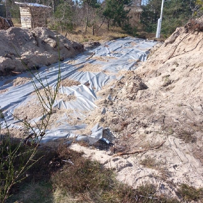Udgravning dækket med plast og sand i naturen